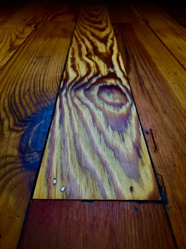 New pine board laid into a gap among older stained heart pine boards