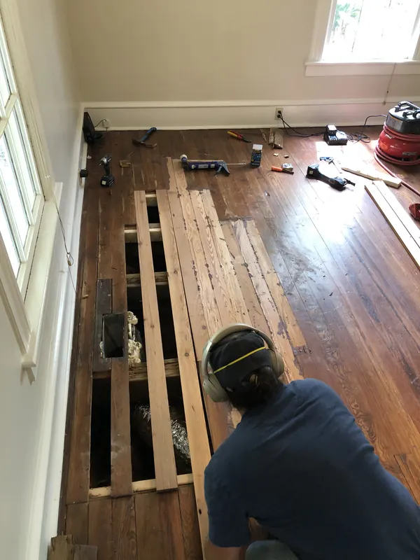 Craftsman kneeling to place reclaimed boards with a pry bar and hammer