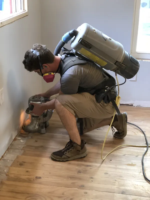 Craftsman crouching with a sander and backpack vacuum