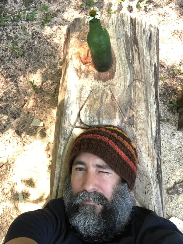 Bearded man in a knit cap standing beside weathered timber