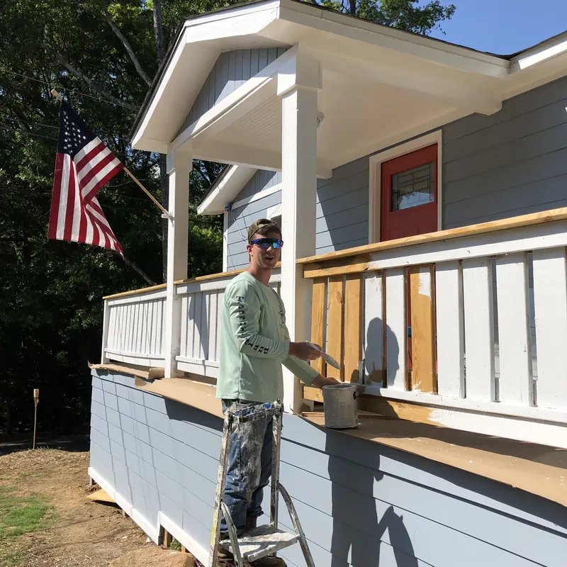 Craftsman standing on a porch beside an American flag
