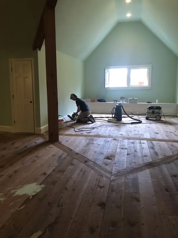Craftsman sanding a wide floor in a green attic room