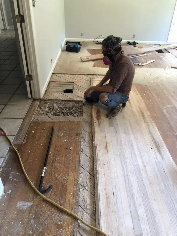 Craftsman kneeling to repair floorboards beside old tile