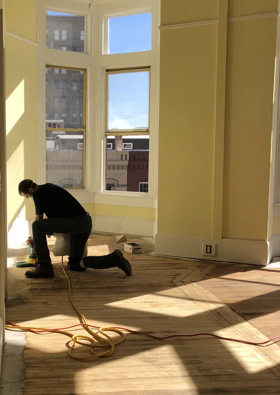 Craftsman kneeling to work on flooring in a sunlit bay