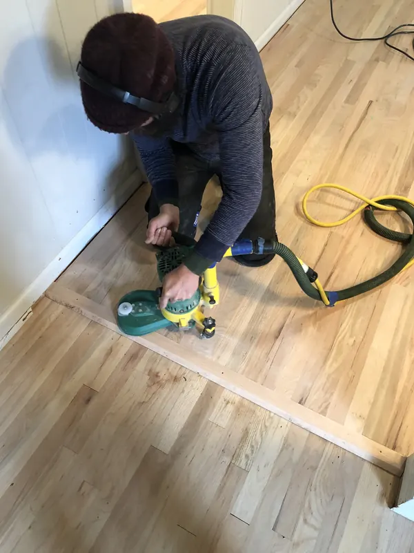 Craftsman crouching with an orbital sander on pale oak