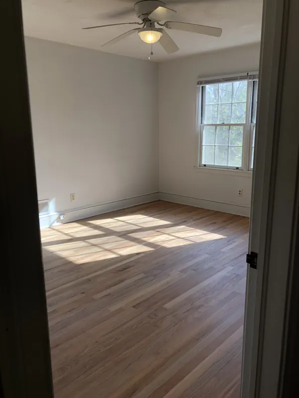 Empty bedroom with warm oak floor and a sunlit window