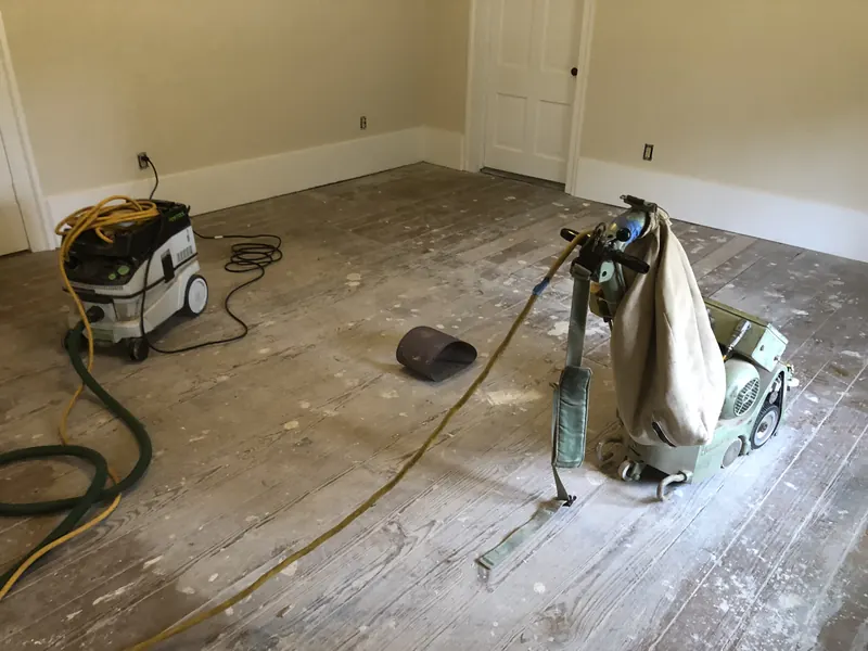 Empty room with bare subfloor and sanding equipment