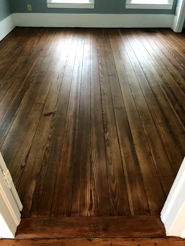 Deep brown heart pine floor with a sunlit window beyond