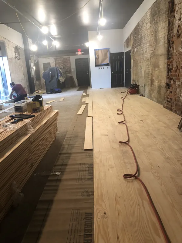 Long room with flooring being laid toward brick wall