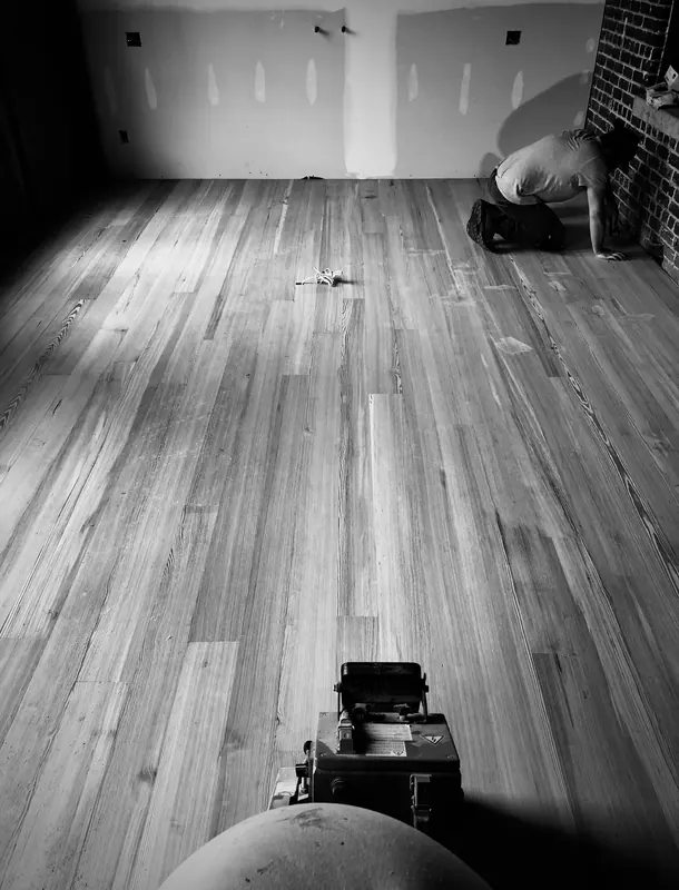 Black and white view of a wide plank floor and sander