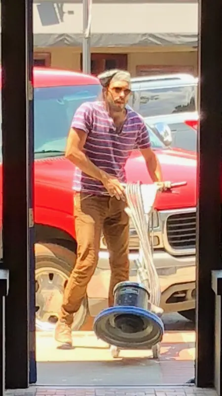 Man wheeling a floor sander past a red truck