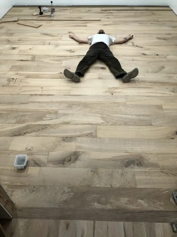 Person lying flat on a finished floor, arms outstretched